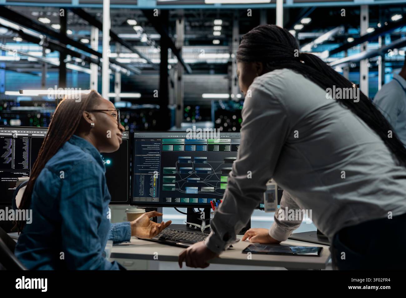 Server facility supervisor supervising technical work from systems engineer applying AI neural network models. Stock Photo