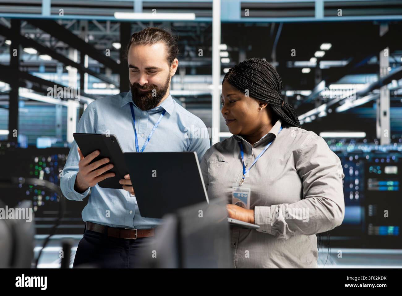 Smiling data center team works with digital devices while reviewing systems, scripts and server infrastructure. Stock Photo