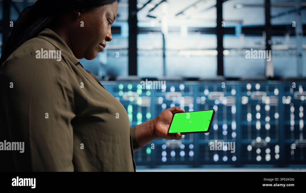 Data center administrator works with a chroma key smartphone, using an editable screen to watch a technical tutorial. Stock Photo