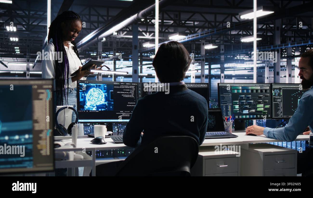 Technicians in high tech high tech server room cooperate on neural network software development, while IT staff members talking, implementing deep learning technology working with computer. Stock Photo