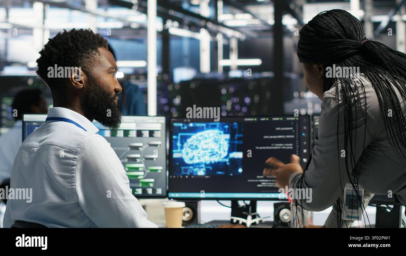 Server room supervisor overseeing work done by engineer working with deep learning models to review data sets. Stock Photo