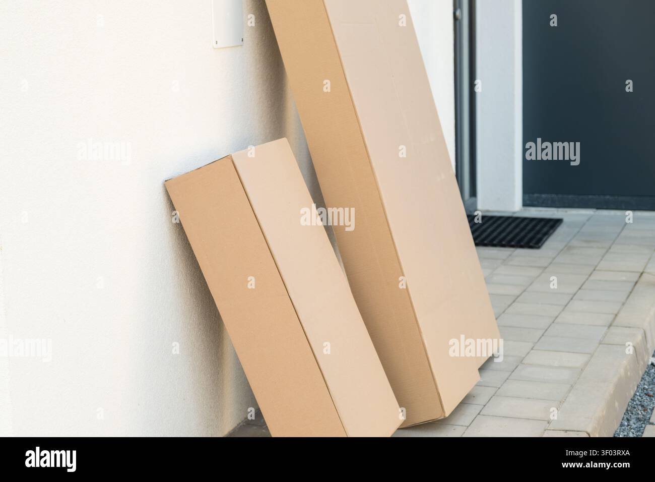 Two brown cardboard delivery boxes leaning against a wall near the front door of a home.  Stock Photo
