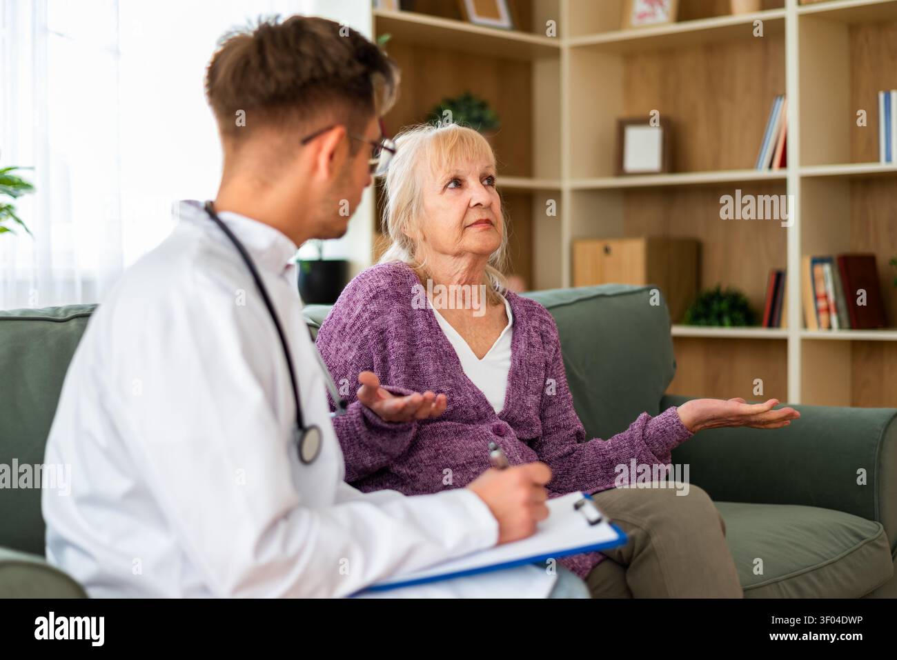 A healthcare professional carefully documents an elderly patient's concerns as she discusses her health issues during an in-home medical appointment. Stock Photo