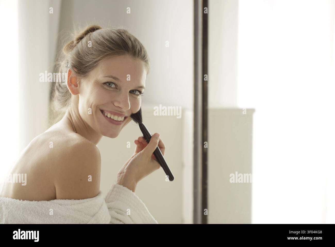 Smiling woman in a robe applying makeup Stock Photo