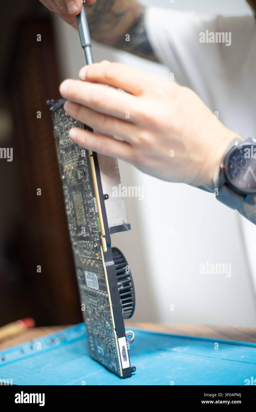 Person repairs a computer graphics card in a workshop during the day using tools for maintenance and improvement Stock Photo