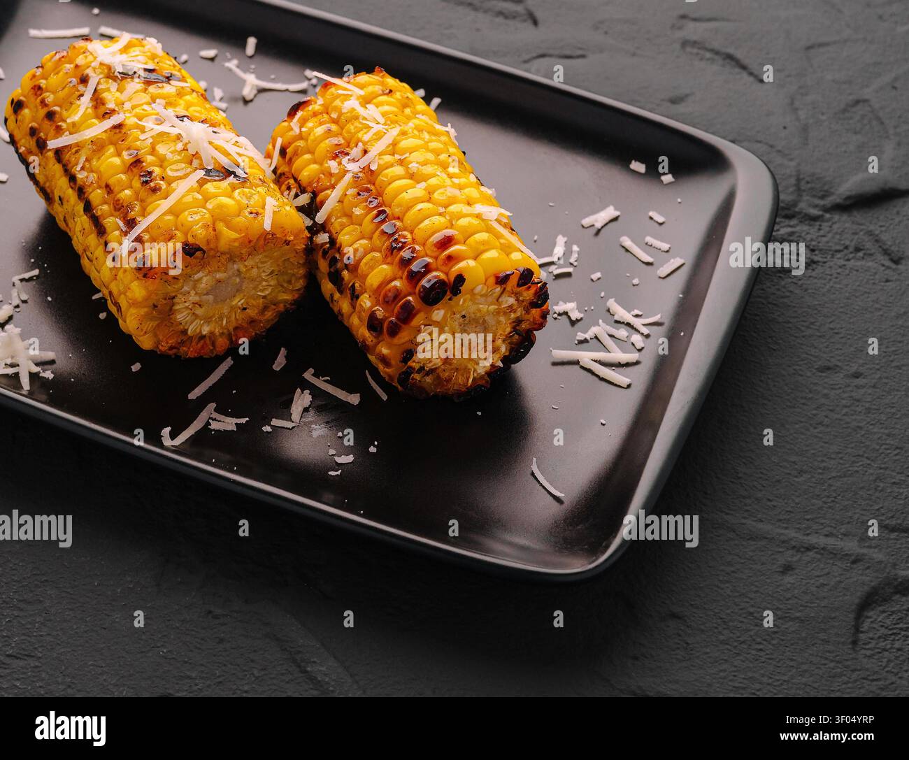 Grilled corn cobs topped with grated cheese, presenting a delicious summer snack Stock Photo