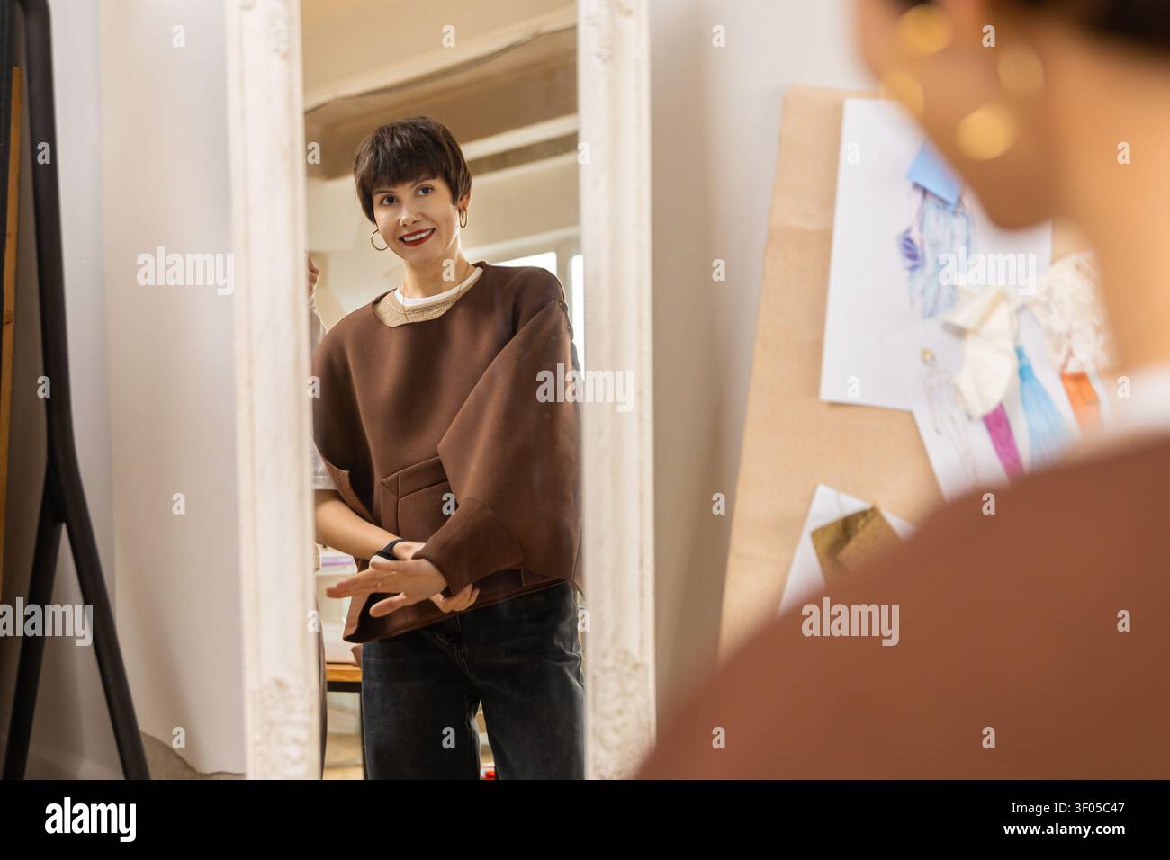 Designer looking in mirror while adjusting brown top Stock Photo