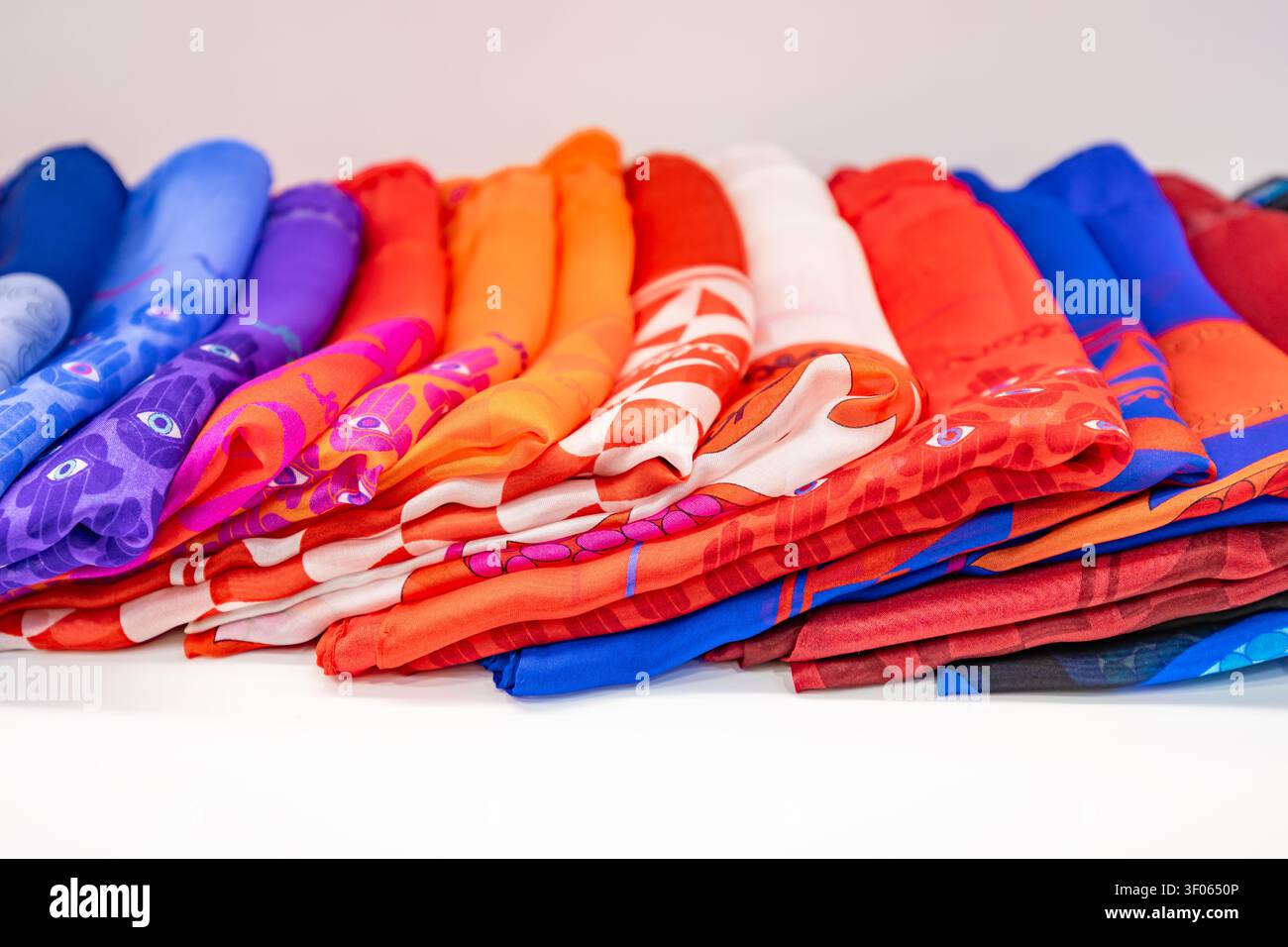 Large row of colorful silk scarves with vibrant abstract patterns arranged on white background Stock Photo