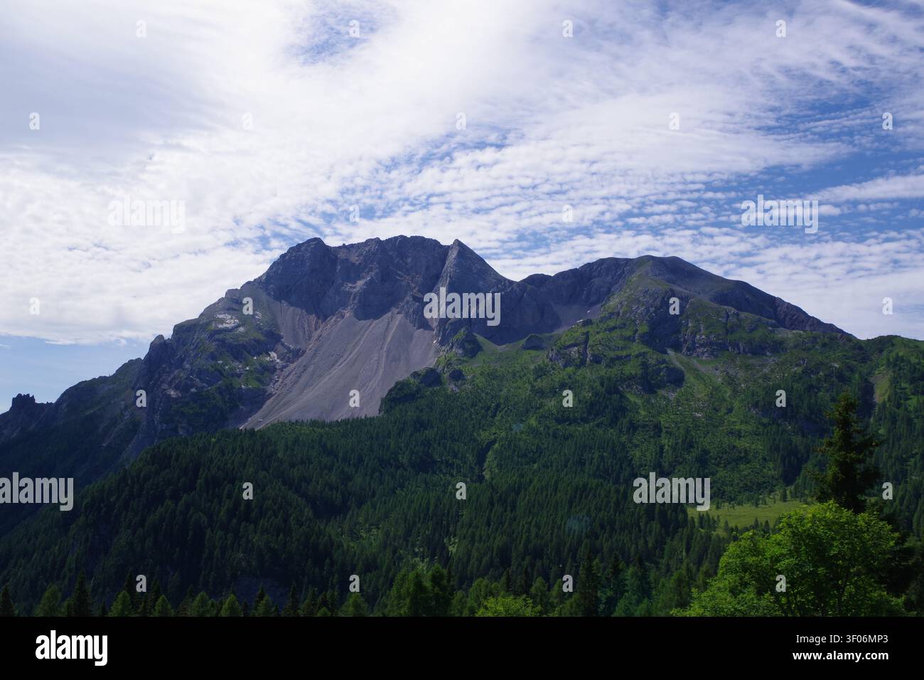 Mountain Peak Above Forested Valley Under Dramatic Cloudy Sky Stock Photo