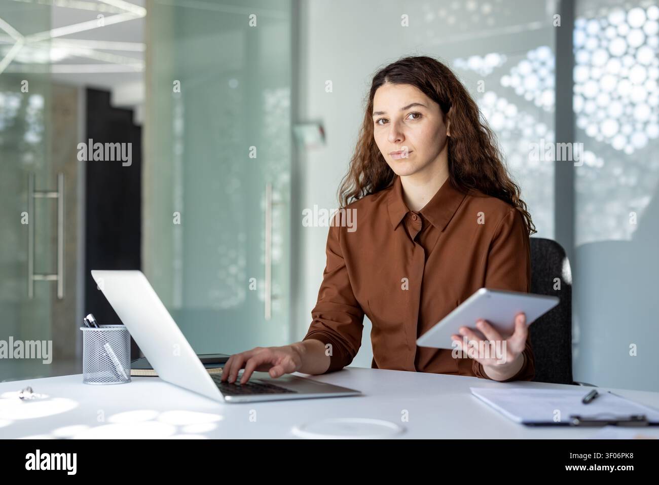 Young businesswoman multitasking with laptop and digital tablet in modern office Stock Photo