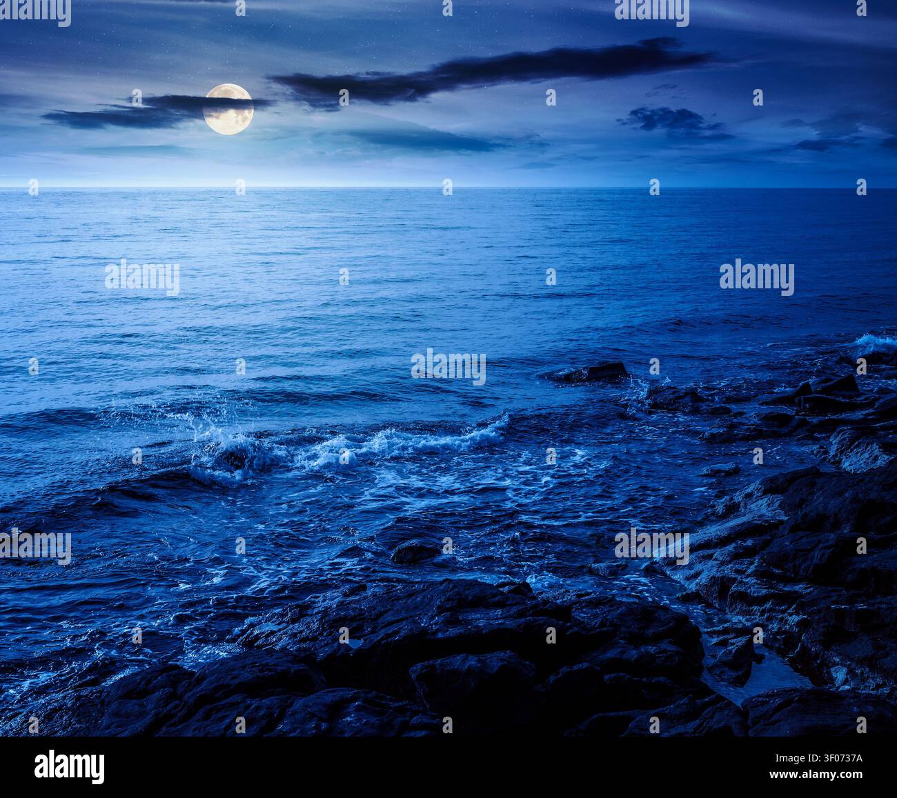 sea coast with stones and rocks at night. summer vacation background. full moon over seascape with rough terrain. fantasy relaxing at the sea. mysteri Stock Photo