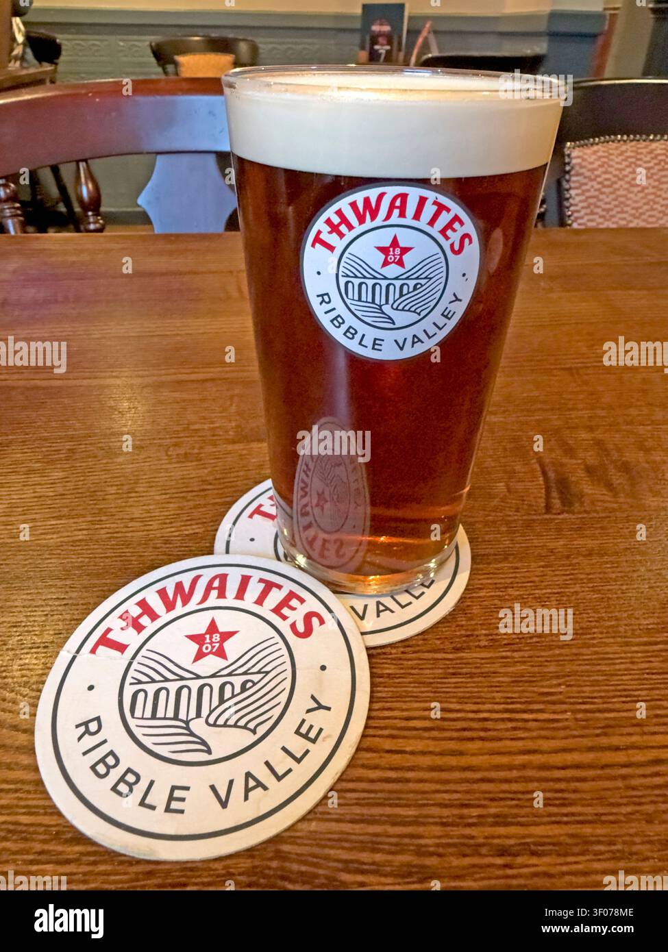 Full Pint of head-on Thwaites Ribble Valley Amber ale with branded beer mat on a pub table in Lancashire, England, UK. Stock Photo