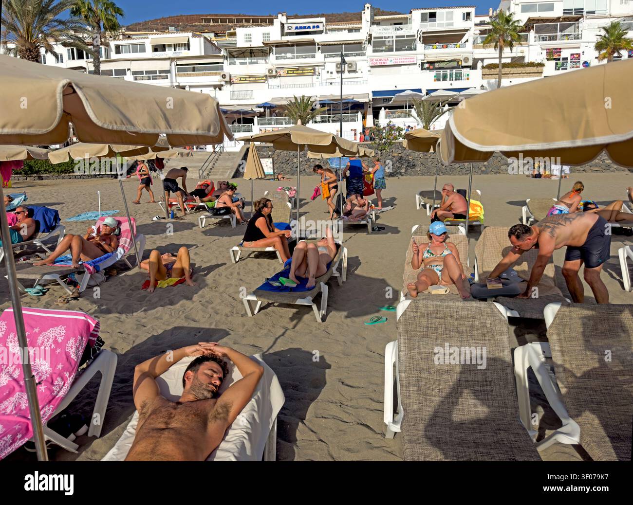 Northern European and Russian holidaymakers crowd the dark-sand beach at Los Cristianos, Tenerife, during a winter-sun break. Stock Photo