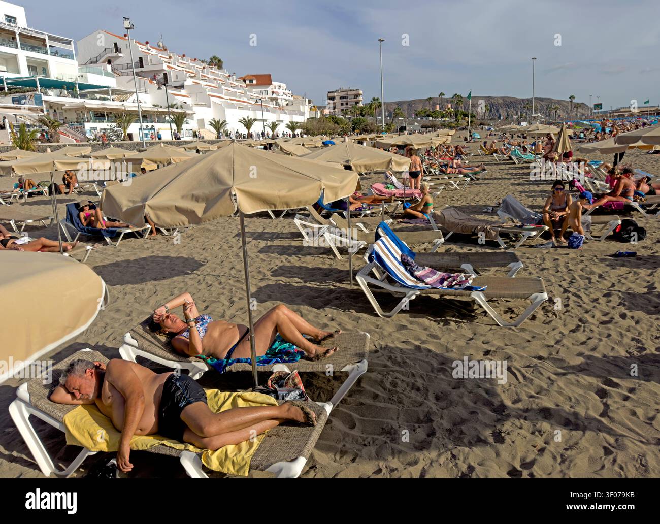 Northern European and Russian holidaymakers crowd the dark-sand beach at Los Cristianos, Tenerife, during a winter-sun break. Stock Photo