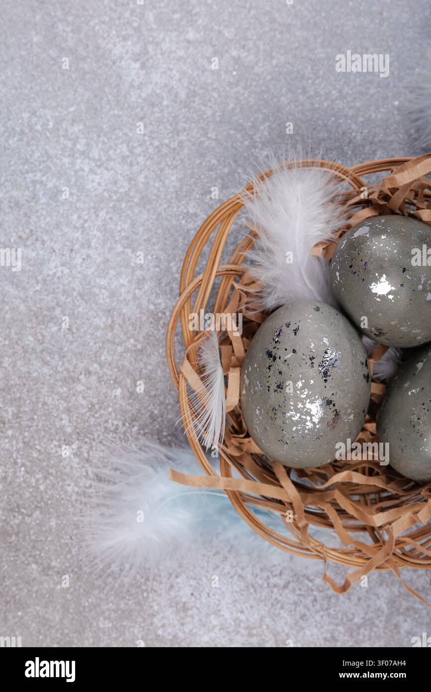 Easter eggs in wicker nest with feathers on gray background Stock Photo
