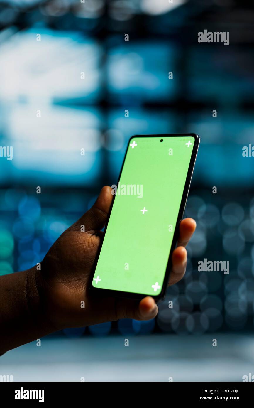 Data center engineer works with a chroma key smartphone, using an editable screen to review performance data. Stock Photo
