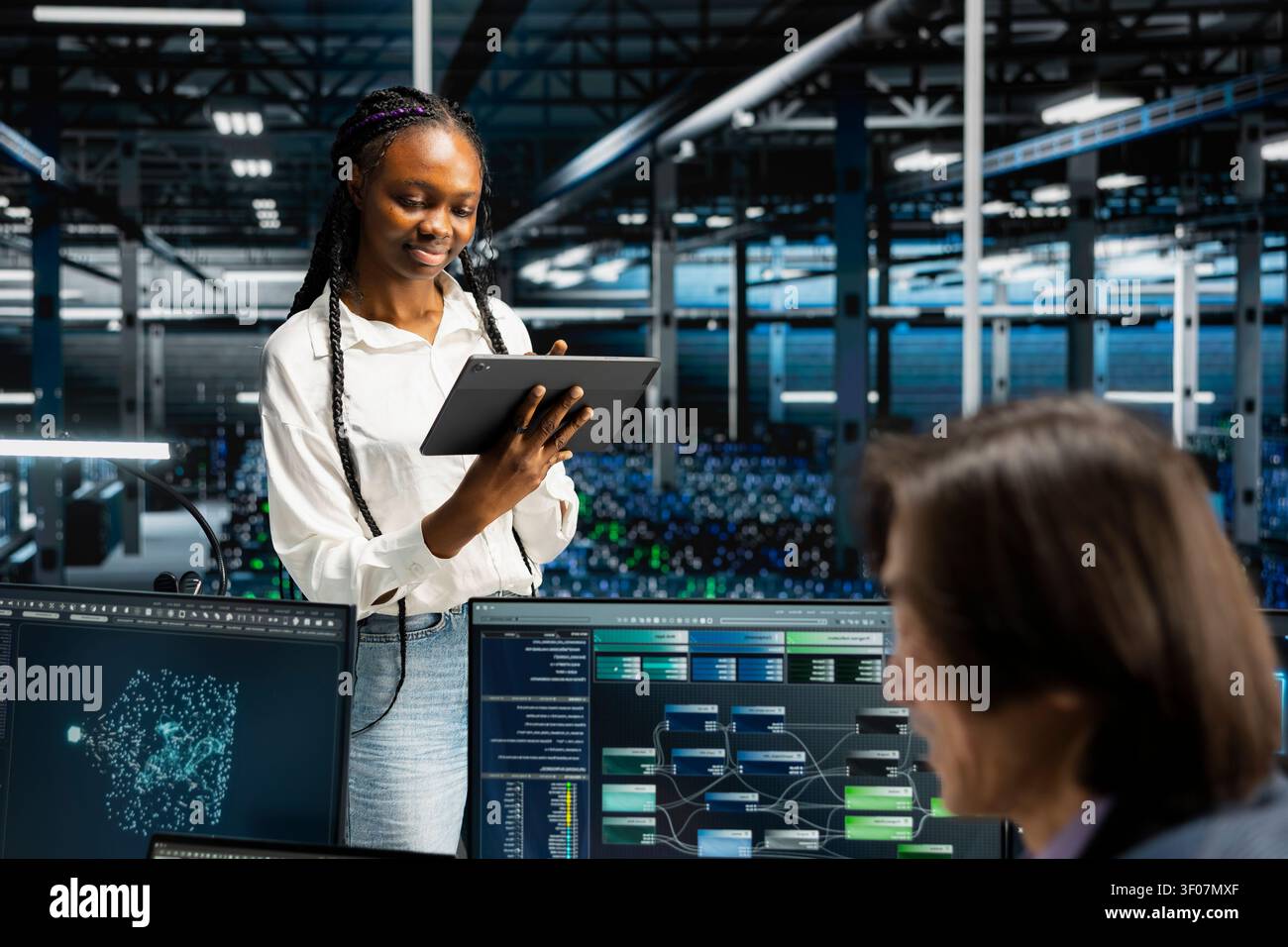 Cheerful server facility software engineer working with digital tablet, coding, supervising systems for uptime and efficiency. Stock Photo