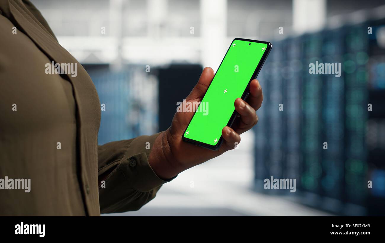 Server facility software engineer works with green screen mobile mobile device to watch video tutorial on how to update rig. Stock Photo