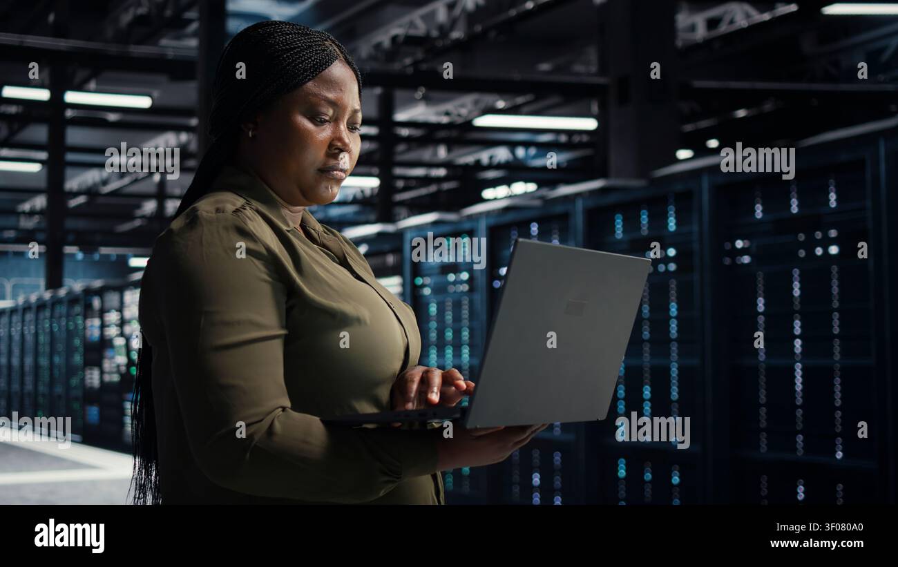Software engineer in server facility working with notebook computer to update systems for increased stability. Stock Photo