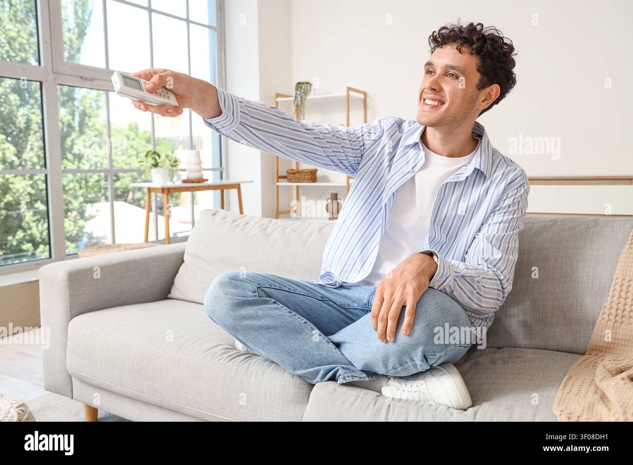 Young man using remote control on sofa in living room Stock Photo