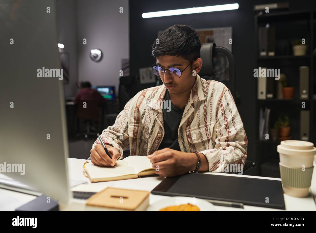 Asian Gen Z Man Taking Notes at Desk during Evening Study Stock Photo
