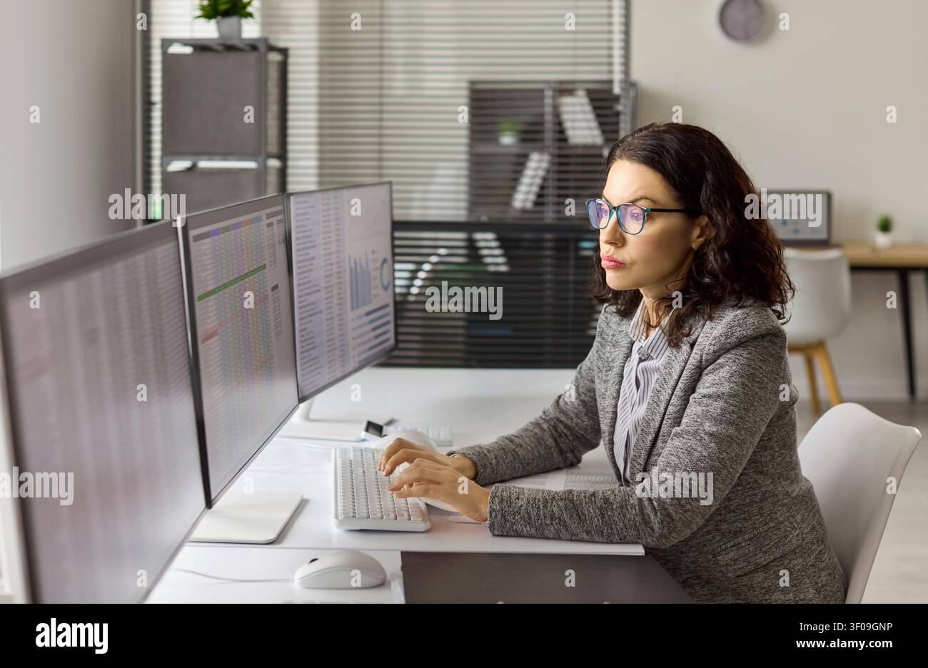 Accountant analyzing finance data on multiple monitors in modern office workspace Stock Photo