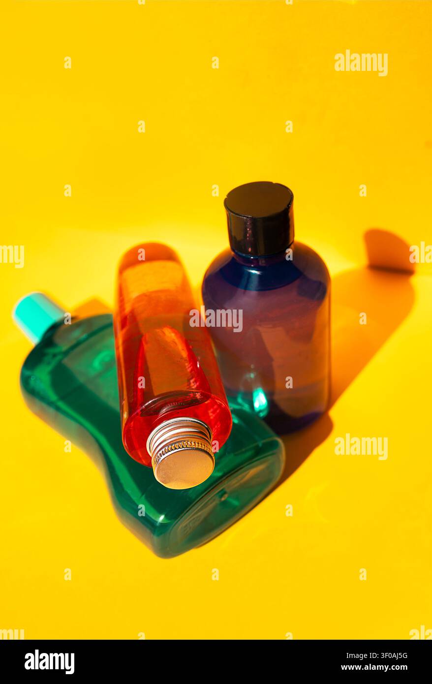 Three plastic bottles in different shapes and colors are arranged on a yellow background, featuring green, red, and blue hues with distinct caps Stock Photo
