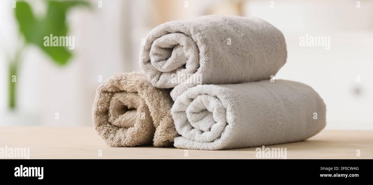 Three rolled soft towels stacked on wooden surface Stock Photo