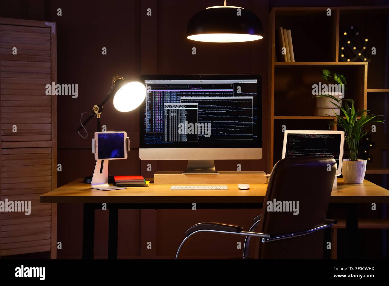 Modern workspace with computer screens displaying code at night Stock Photo