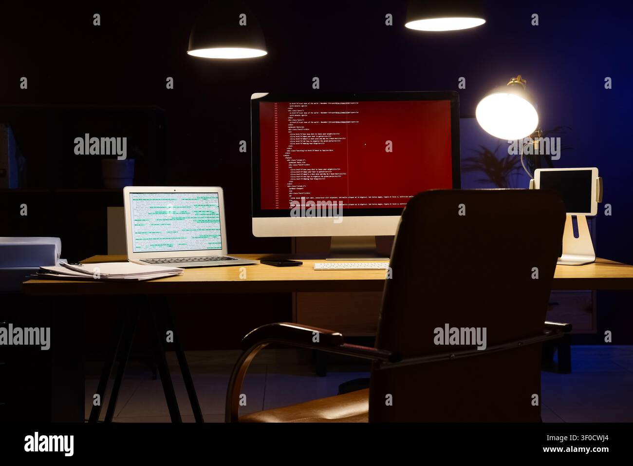 Modern workspace with computer screens displaying code at night Stock Photo