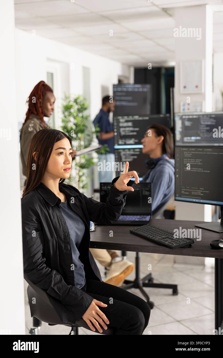 Woman developer interacts with holographic screen in futuristic office. Female programmer testing web development code on virtual interface, representing innovation and advanced digital technology. Stock Photo