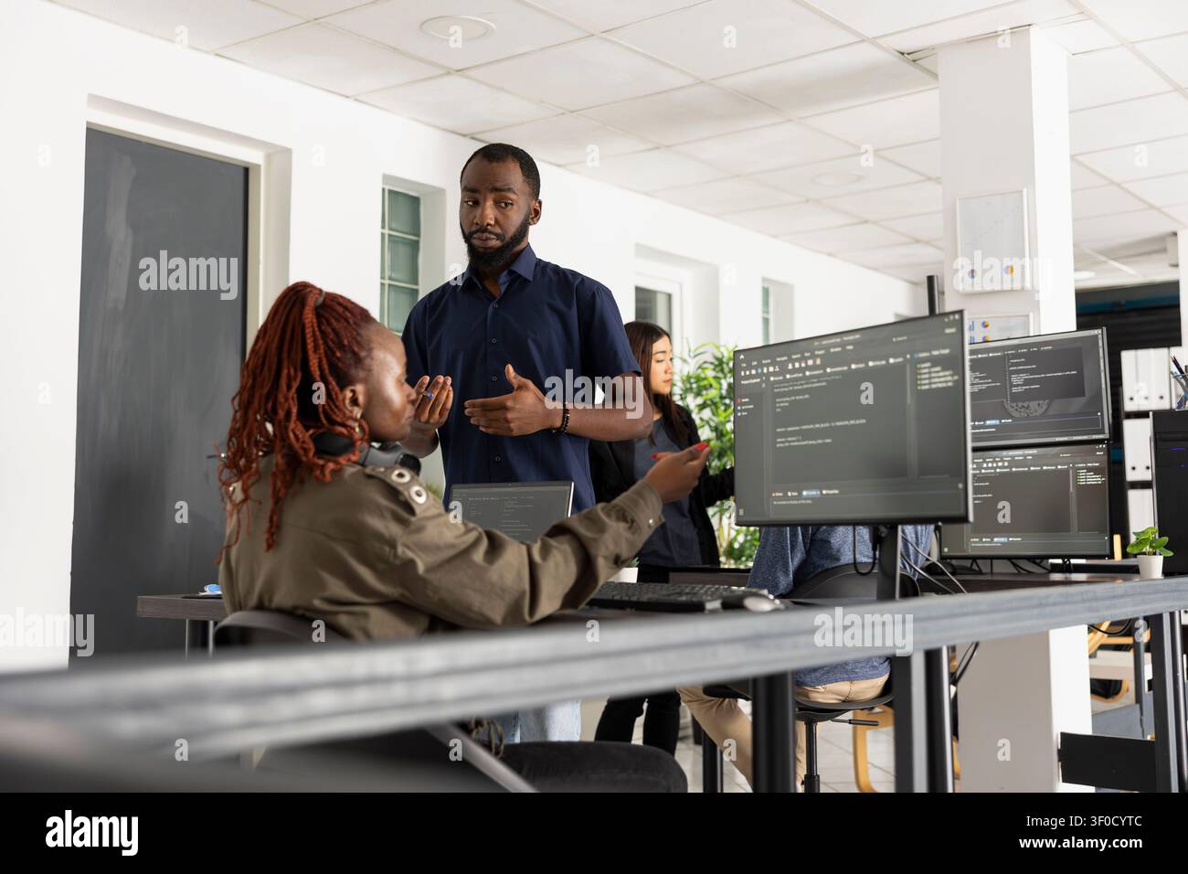 African American developers work together in startup office, comparing website code on desktop pc. Focused programmers discuss strategy, technology and collaborative digital problem solving. Stock Photo