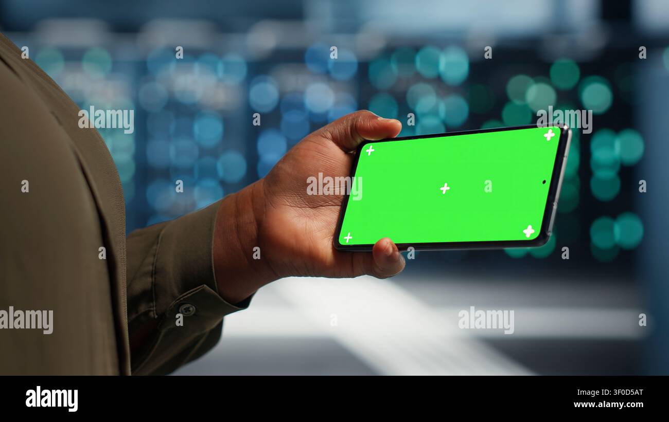 Data center administrator works with a chroma key smartphone, using an editable screen to watch a technical tutorial. Stock Photo