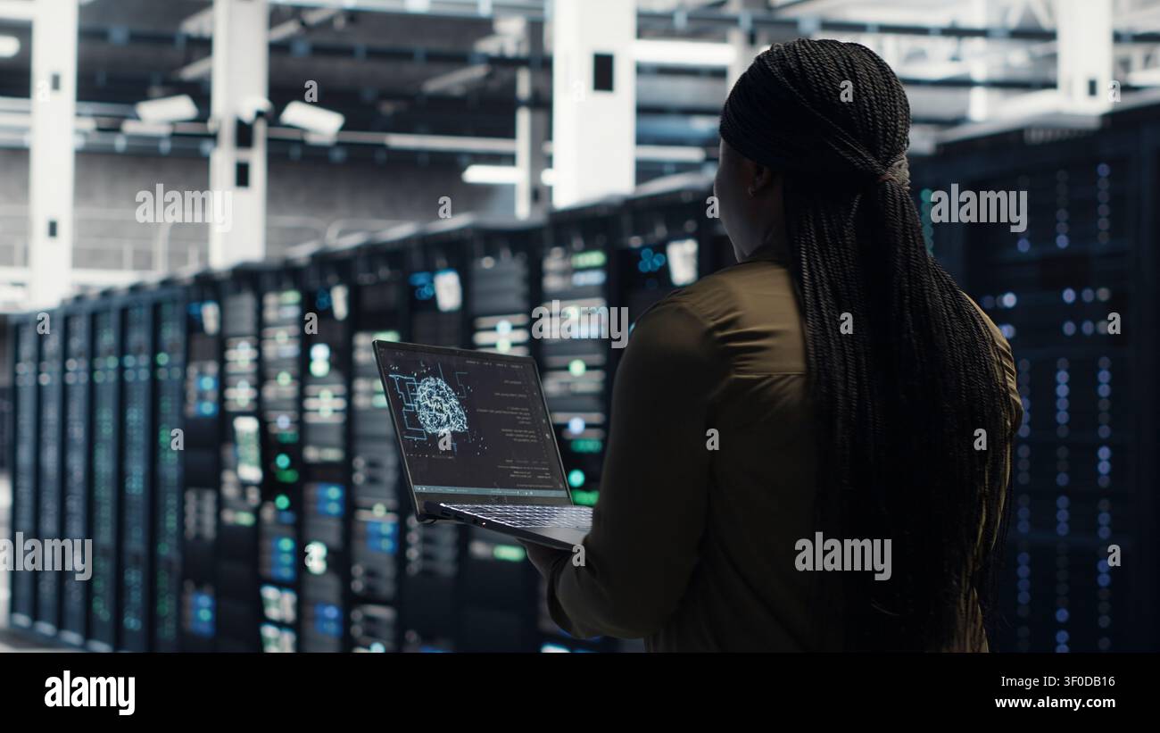 Software developer uses laptop-based deep learning tools in a server room to improve AI operations and system efficiency. Stock Photo