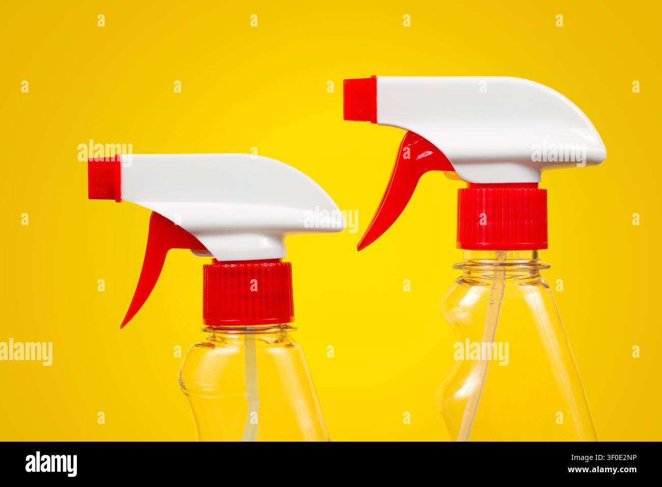 Close-up detergent sprayers on a yellow background. Two red and white sprayers. Stock Photo