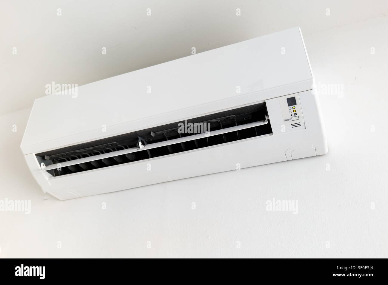 Wall-mounted split air conditioner unit on white wall, indoor climate control Stock Photo