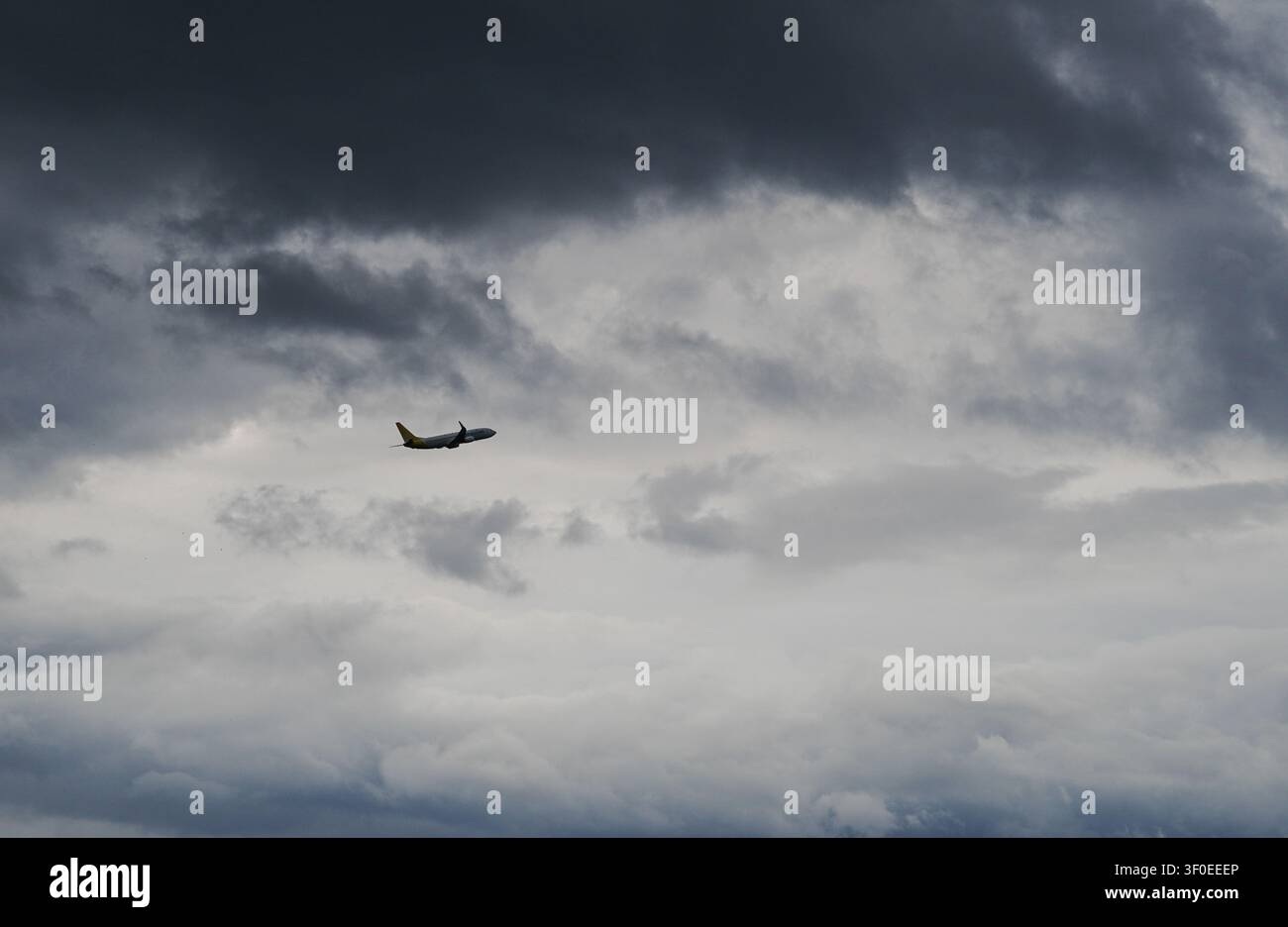 Passenger airplane flying high through a dramatic, cloudy dark sky at sunset Stock Photo