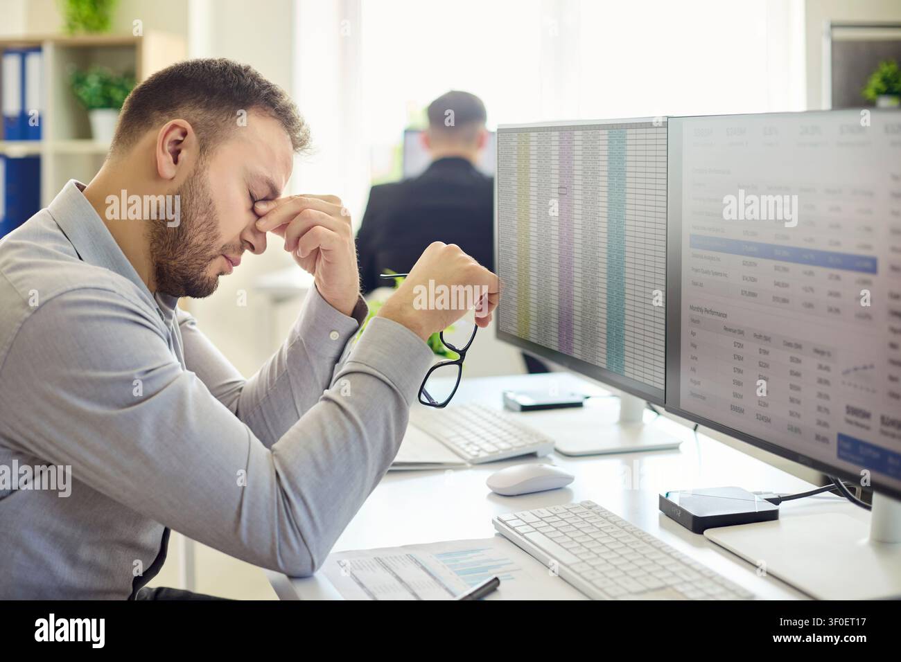 Stressed employee man at computer with spreadsheets suffering burnout fatigue Stock Photo