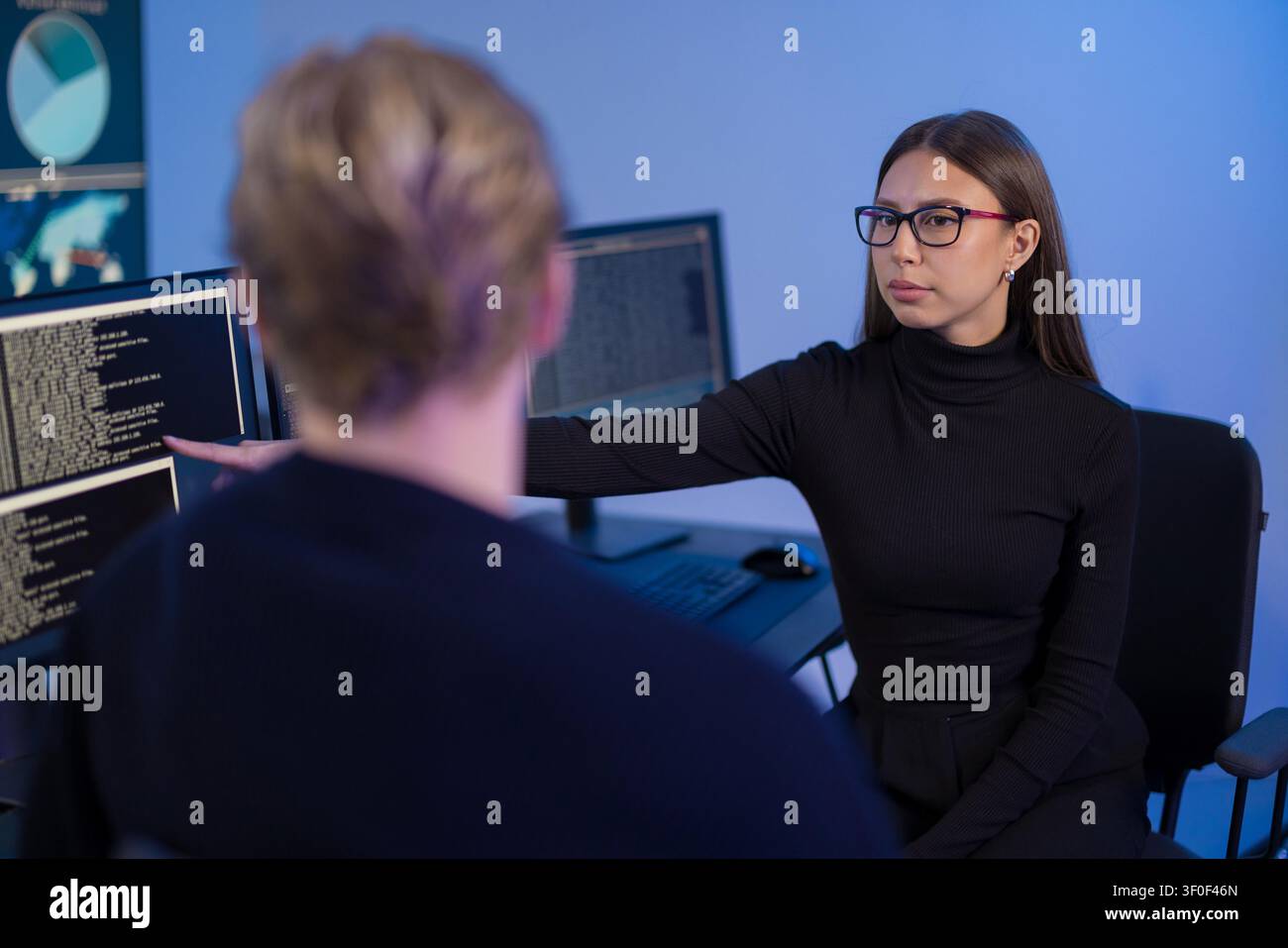 IT professionals collaborating in a secure operations center with code displayed on screens Stock Photo