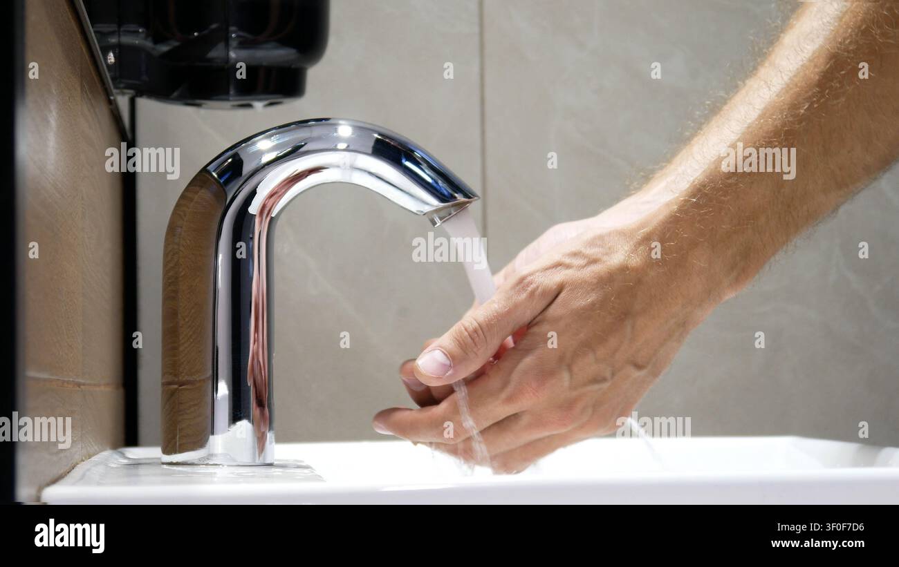 A man washes his hands using a touchless faucet close-up Stock Photo