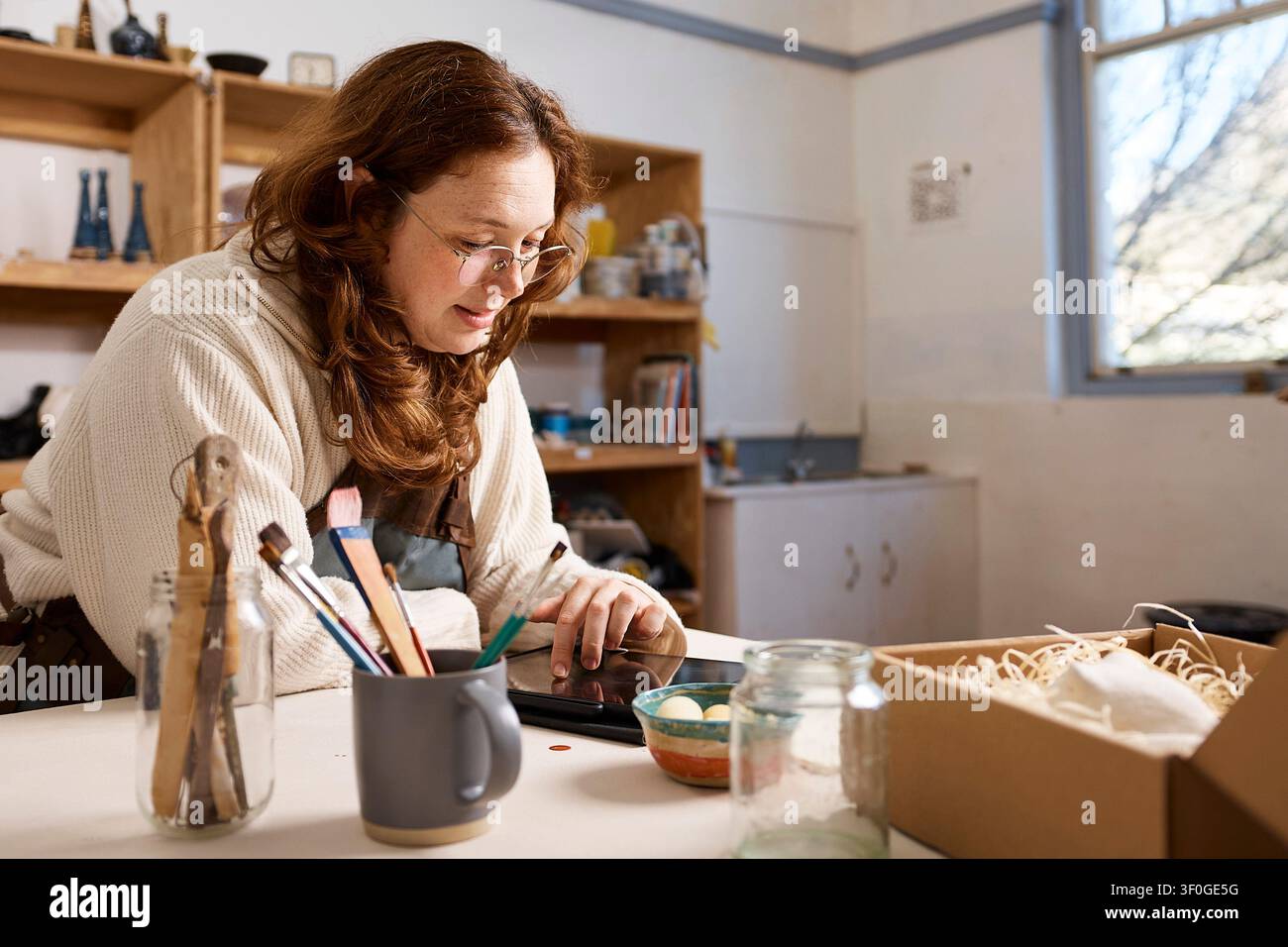 Small Business Pottery Studio Owner Packing Handmade Ceramics While Using Tablet in Workshop Stock Photo