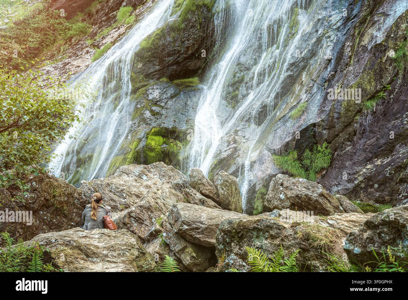 Woman sitting on rocks looking at Powerscourt Waterfall in County Wicklow Ireland scenic nature landscape. Stock Photo