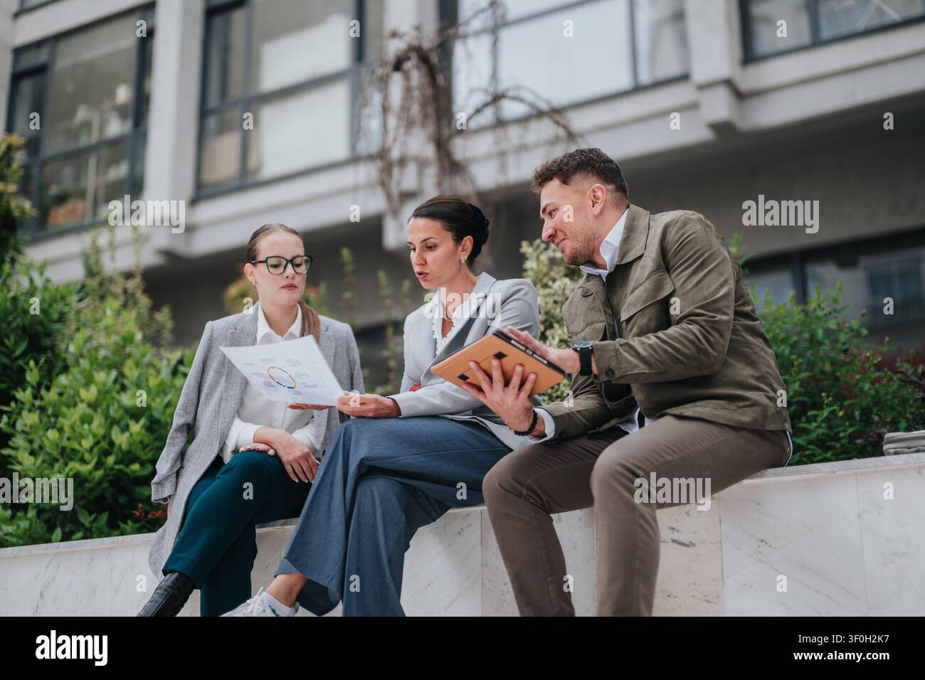 Three colleagues having a business meeting outdoors reviewing documents and a tablet Stock Photo