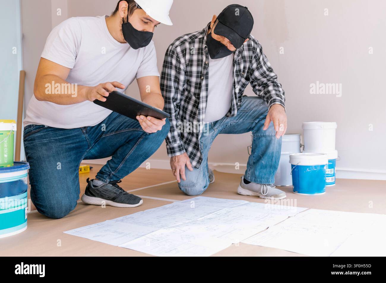 Construction workers collaborating on renovation plans, checking blueprints and a digital tablet for project details Stock Photo