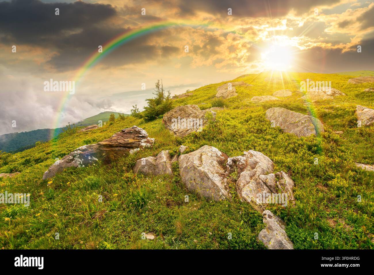 sunset over green landscape of mountain in summer. view of rock among grass on the hillside. travel background under a cloudy sky. mountain scenery wi Stock Photo