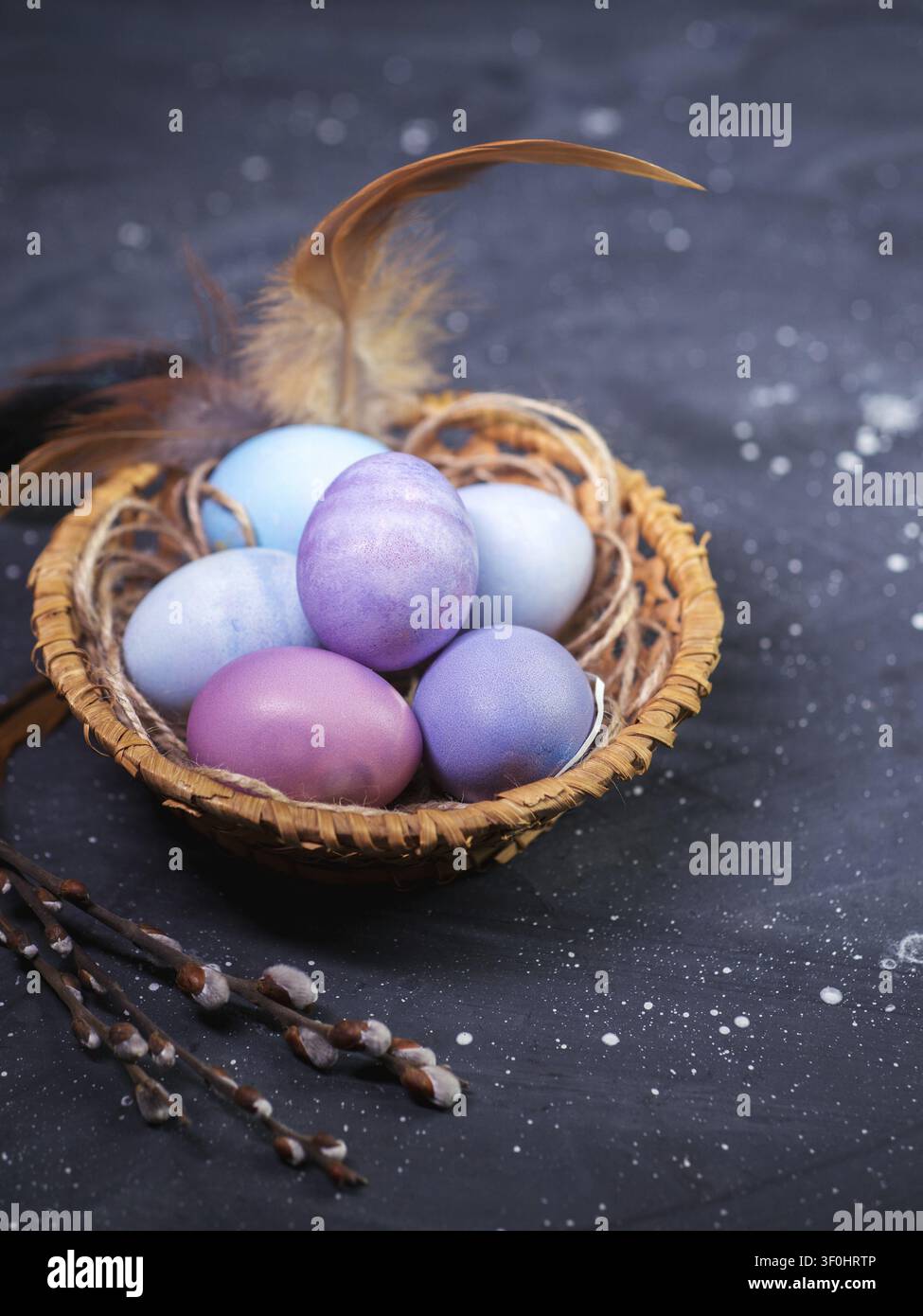 Pastel-colored Easter eggs in a wicker basket on a dark table, willow branches Stock Photo