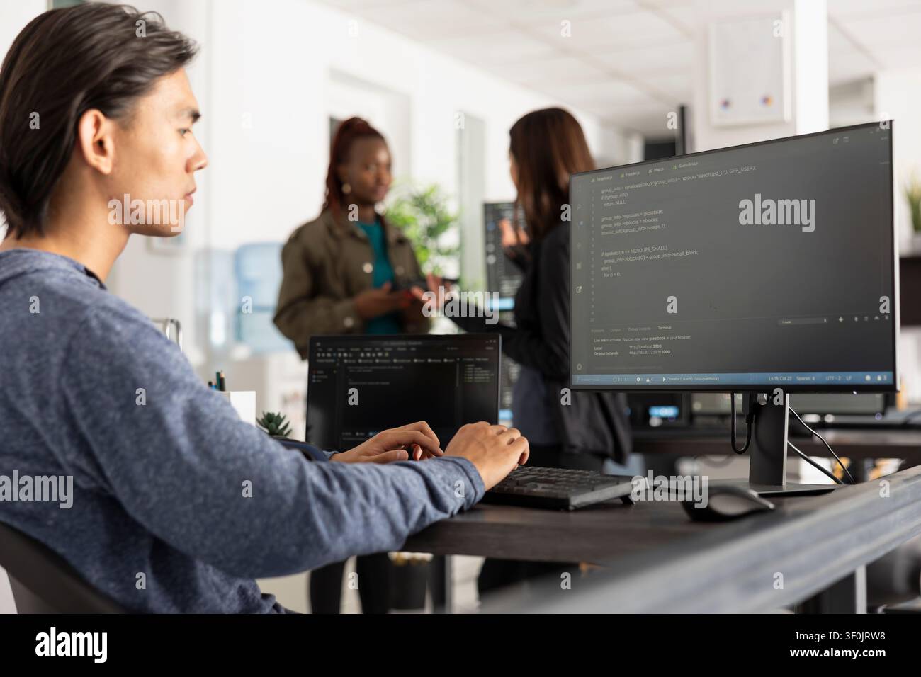Focused software developer typing at desktop pc in office. Programmer diligently works on web development tasks, demonstrating concentration and commitment to completing coding projects efficiently. Stock Photo