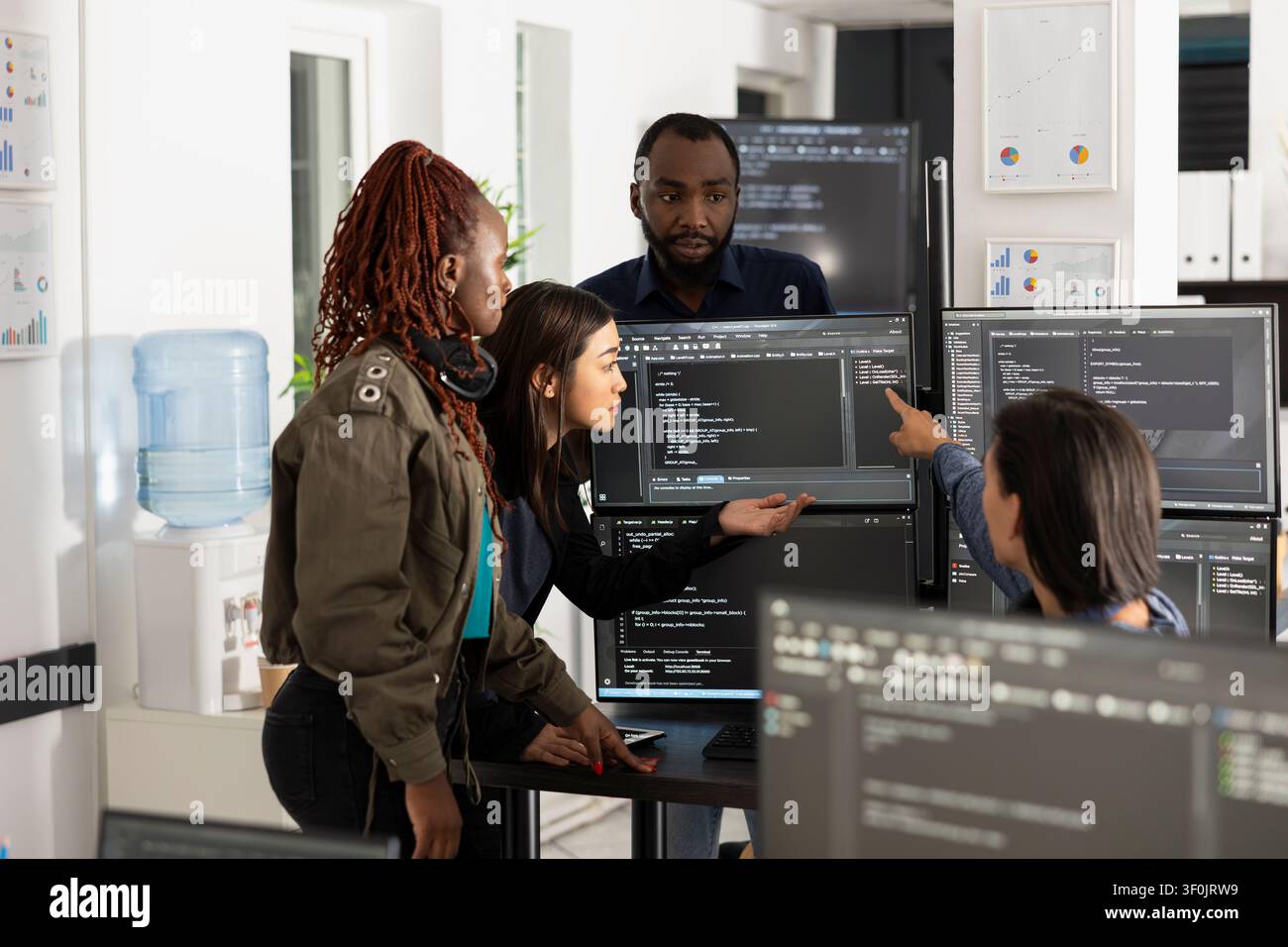 Diverse group of software developers in modern office collaborating, discussing and analyzing source code on multiple computer monitors, working together on web development project. Stock Photo