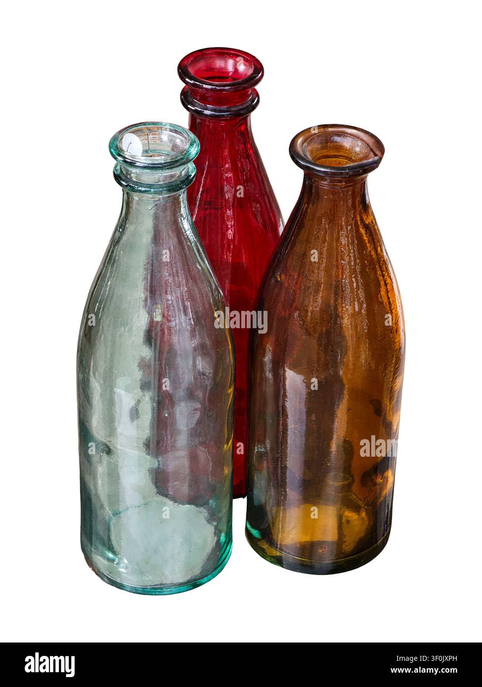 Three empty glass bottles in different colors stand together against a white background. These bottles can be used for various purposes in home decor Stock Photo
