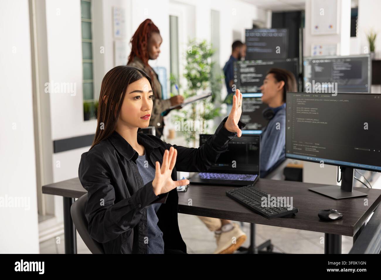 Asian female programmer works with 3d interface in office, testing code for web development. Woman developer with arms raised, interacting with holographic screen and analyzing frontend data. Stock Photo